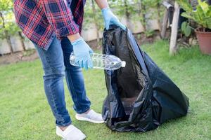 Mulher asiática voluntária transportar garrafas de plástico de água para o lixo do saco de lixo no parque, conceito de ecologia de ambiente de resíduos de reciclagem. foto