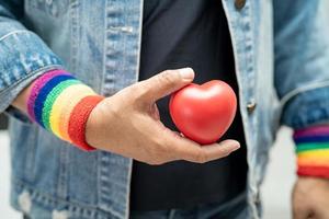 senhora asiática usando pulseiras de bandeira de arco-íris e segurar um coração vermelho, símbolo do mês do orgulho LGBT, comemorar anual em junho social de gays, lésbicas, bissexuais, transgêneros, direitos humanos. foto