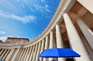 rua colunatas da basílica de peters na cidade do vaticano. guarda-chuva azul harmoniza com o céu foto