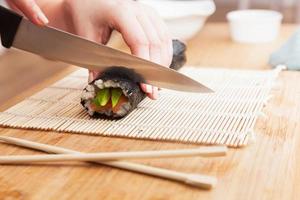 preparando sushi, cortando. salmão, abacate, arroz e pauzinhos na mesa de madeira. foto