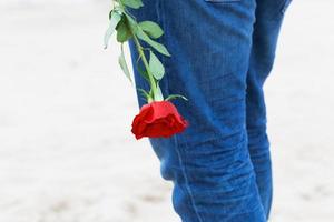 homem com uma rosa nas costas esperando por amor. encontro romântico na praia foto