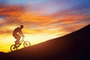 homem andando de bicicleta bmx subindo contra o céu pôr do sol. força, desafio. foto