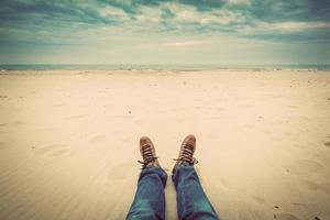 perspectiva de primeira pessoa das pernas do homem em jeans na praia de outono foto