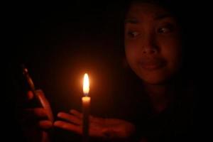 uma mulher asiática chocante apontando o celular na frente da luz de velas na noite escura foto