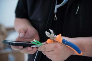 engenheiro eletricista com fio e alicate na mão usando telefone celular foto