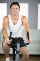 homem bonito apto exercitando na bicicleta sorrindo para a câmera