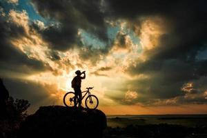 silhueta de um motociclista e bicicleta no fundo do céu. foto