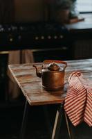 tiro vertical de chaleira de aço na mesa de madeira no quarto aconchegante. antigo bule de alumínio antigo para fazer chá. utensílios domésticos antigos. foto