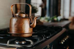 chaleira de bronze na cozinha moderna. antigo bule vintage no fogão a gás. preparando o chá. chaleira de alumínio. luz do dia ensolarado da janela. foto