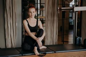 bela jovem treinadora de pilates sentada com os braços em volta das pernas em posição calma e relaxada foto