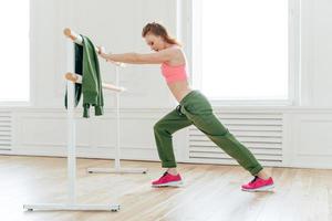 esporte, recreação, conceito de flexibilidade. mulher forte motivada faz prancha, inclina-se na barra de balé, alonga-se antes dos exercícios prepara músculos ou bíceps para treinamento duro. instrutor de aeróbica indoor foto