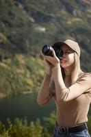 fotógrafo turista viajante em pé no topo verde na montanha segurando nas mãos a câmera fotográfica digital foto