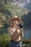 fotógrafo turista viajante em pé no topo verde na montanha segurando nas mãos a câmera fotográfica digital foto