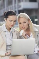 jovens mulheres de negócios trabalhando juntos no laptop enquanto está sentado ao ar livre foto