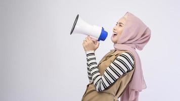 feliz mulher muçulmana está anunciando com megafone em fundo branco foto