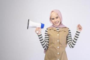 feliz mulher muçulmana está anunciando com megafone em fundo branco foto