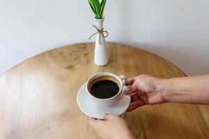 xícara de café preto na mão na mesa de madeira. foto