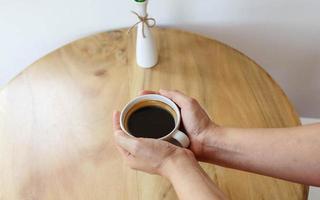 xícara de café preto na mão na mesa de madeira. foto