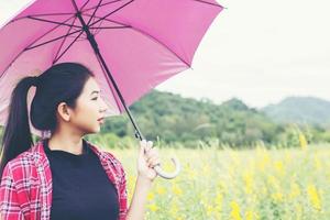 linda jovem segurando o guarda-chuva vermelho no campo de flores amarelas e fundo de montanha. foto