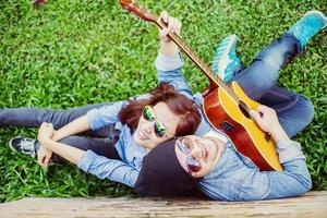 homem hipster tocando violão para sua namorada ao ar livre contra a parede de tijolos, curtindo juntos. foto