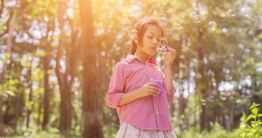 menina bonitinha vestindo uma camisa rosa soprando bolhas no parque, estilo vintage. foto