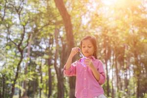 menina bonitinha vestindo uma camisa rosa soprando bolhas no parque, estilo vintage. foto