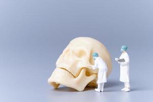 médico de pessoas em miniatura com um crânio humano gigante em um fundo cinza foto