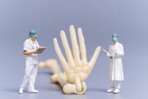 médico de pessoas em miniatura com um osso humano gigante em um fundo cinza foto