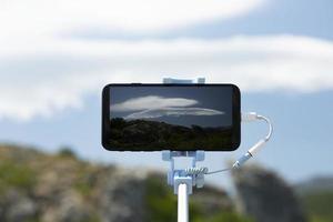 um smartphone em um bastão de selfie fotografa um fenômeno raro, a nuvem lenticular. fotografia móvel durante a viagem. foto