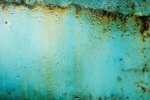 listras de ferrugem em metal velho atrás de vidro pingando após a chuva. foto