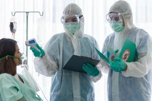 médicos em traje de proteção está monitorando e verificando o paciente infectado com vírus corona ou temperatura covid-19 na sala de quarentena do hospital foto