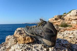 botas de caminhada verde-oliva em um fundo natural de mar e rochas foto