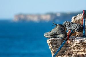 um par de botas de caminhada, verde-oliva em um fundo natural de mar e rochas foto