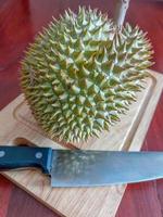 durian verde e faca na tábua de madeira. foto