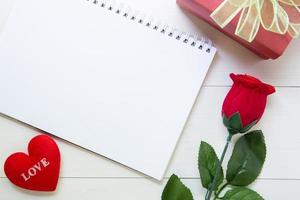 presente presente com flor rosa vermelha e caderno e forma de coração com espaço de cópia na mesa de madeira, 14 de fevereiro de dia do amor com conceito de férias romântico, dia dos namorados. foto