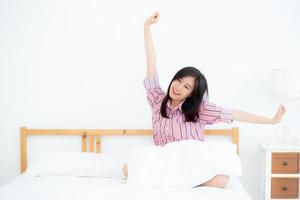 linda de retrato jovem asiática esticar e relaxar na cama depois de acordar de manhã no quarto, novo dia e descansar para o bem-estar, conceito de estilo de vida. foto
