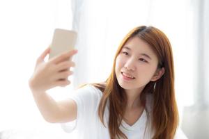 belo retrato jovem mulher asiática tomando uma selfie com telefone celular inteligente no quarto, a garota está fotografando com feliz e sorria com diversão, conceito de estilo de vida. foto