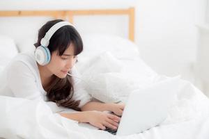 bela jovem asiática deitada no quarto usando o computador portátil mostrando o bate-papo por videochamada em casa, a garota cumprimenta e ouve e fala o conceito de mensageiro, comunicação e estilo de vida. foto