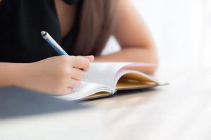 closeup mão mulher asiática sentado estudo e aprendendo a escrever caderno e diário na mesa na sala de estar em casa, lição de casa menina, mulher escritora de negócios trabalhando na mesa, conceito de educação. foto