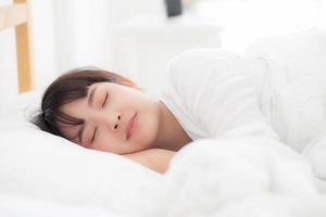 bela jovem asiática dormindo deitada na cama com a cabeça no travesseiro confortável e feliz. menina com relax para o conceito de saúde. foto