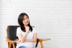 belo retrato jovem asiática confiante pensando com fundo de cimento e concreto, menina sentada na cadeira expressão séria ou dúvidas com ideia, conceito de estilo de vida. foto