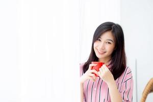 linda de retrato jovem mulher asiática com bebida uma xícara de café em pé fundo de janela de cortina no quarto, garota relaxa de manhã em casa, conceito de estilo de vida. foto