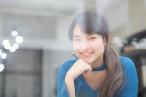 bela jovem escritora asiática sorrindo pensando a ideia e escrevendo no caderno ou diário com feliz, estilo de vida da menina asiática é estudante, planejamento feminino de trabalho, educação e conceito de negócios. foto