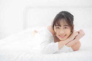 belo retrato jovem asiática deitada e sorrir enquanto acorda com o nascer do sol de manhã, beleza linda garota feliz e alegre descansando na cama no quarto, estilo de vida e conceito de relaxamento. foto