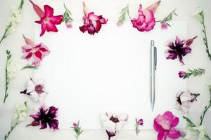 flores de azaleia rosa, flores brancas asystasia gangetica, manjericão verde e folha de papel em branco e caneta em um fundo rosa, papel em branco para sua vista text.top, espaço para texto, configuração plana. foto