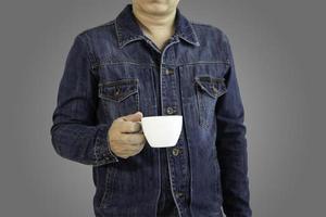 um homem de camisa jeans segurando uma caneca de café ou chá branco contra um fundo cinza gradiente com foco path.selective de recorte. foto