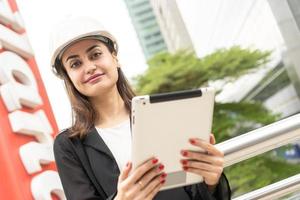 trabalhador engenheiro vestindo uniforme de segurança e capacete usa computador tablet. feliz mulher bem sucedida. mulheres de negócios trabalhando com lista de verificação de tablet, mulher trabalhando foto