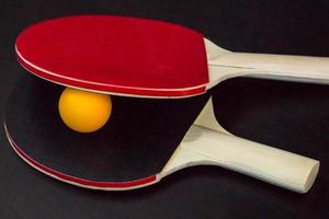 duas raquetes de tênis de mesa ou ping pong e bola em um fundo preto foto