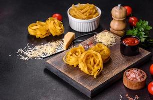 pasta de tagliatelle cru com queijo ralado, tomate cereja, especiarias e ervas em uma tábua de madeira foto