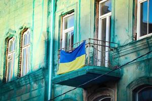 bandeira ucraniana azul e amarela pendurada na varanda de um prédio antigo coberto com rede verde para reconstrução foto